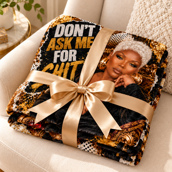Folded Don’t Ask Me for Shit flannel blanket tied with a gold ribbon bow on a cream chair